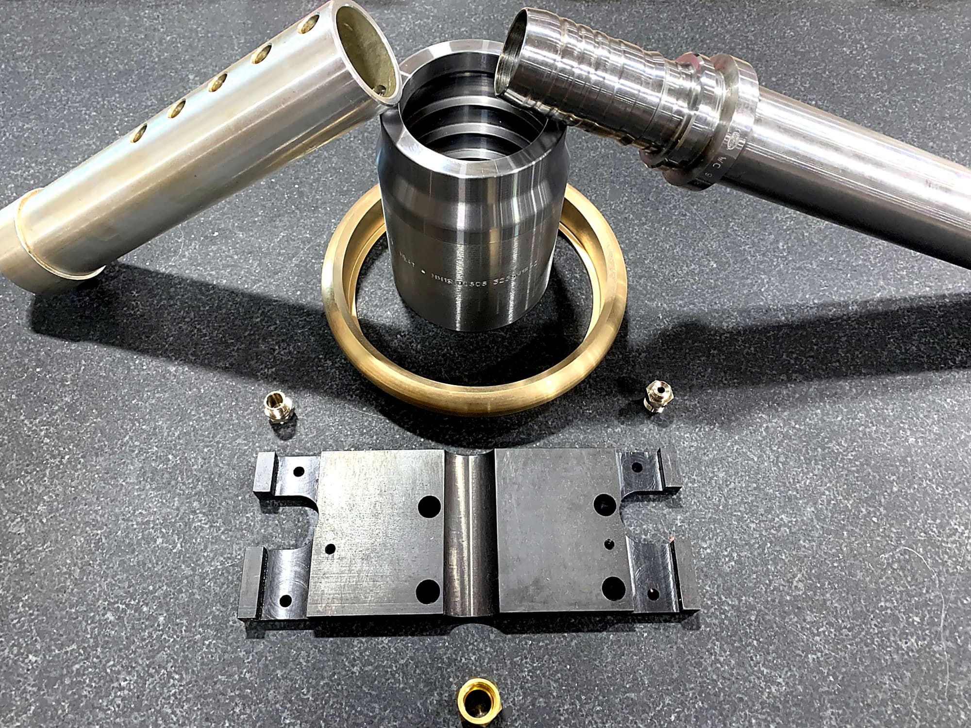 Machined assembly components displayed on a dark surface.